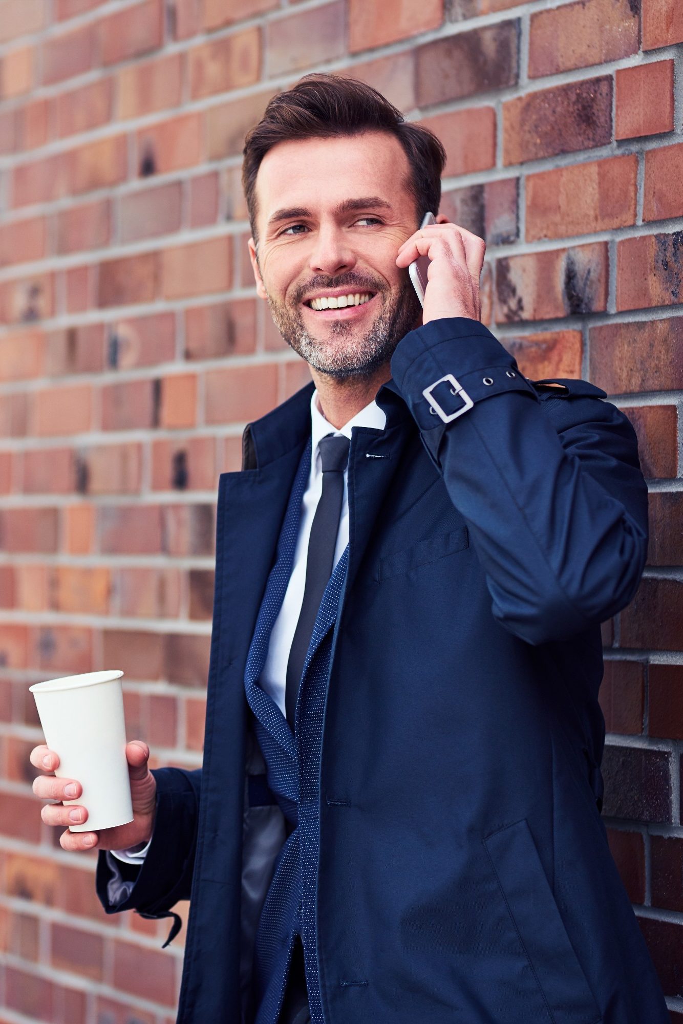 Middle-aged business executive making phone call while enjoying a cup of coffee outside